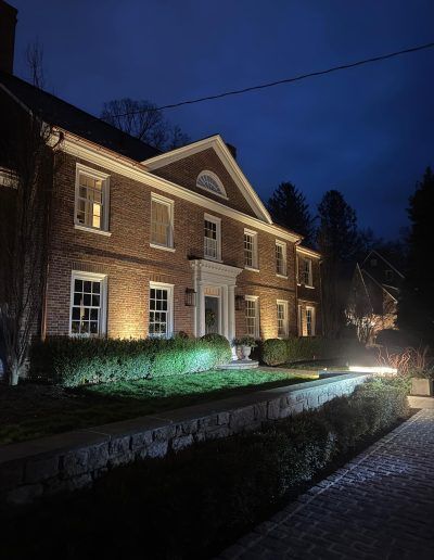 Lit-up brick house at night; landscaping and path illuminated, with a dark blue sky.