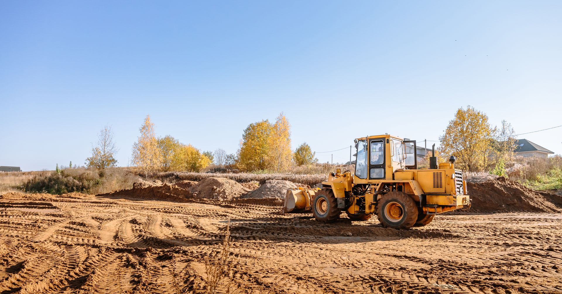 A large yellow wheel loader clearing and leveling land for new building construction.