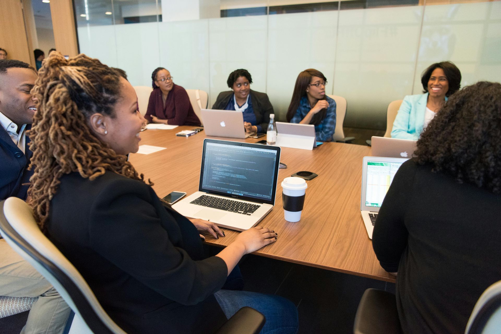 Group of diverse people in business attire at a conference table, working on laptops and smiling.