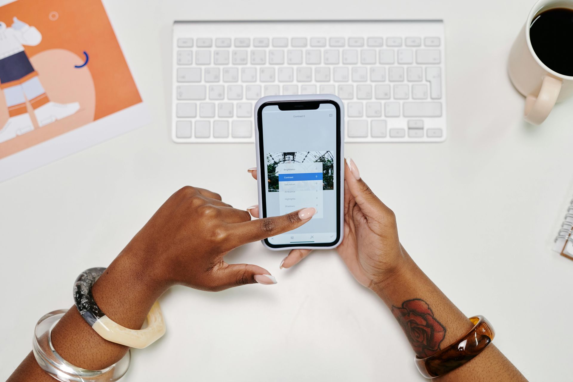 Hands holding phone, scrolling through options on white desk with keyboard and mug.