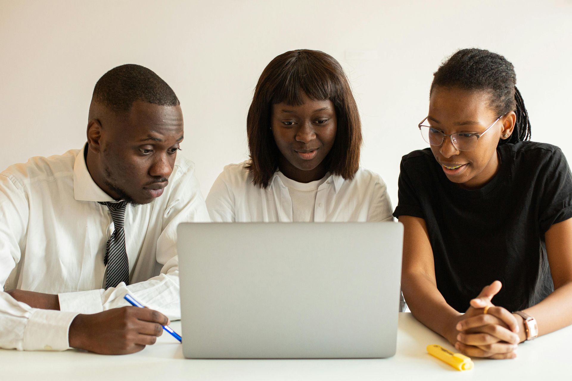 Three Black coworkers look intently at a laptop screen, discussing a project.