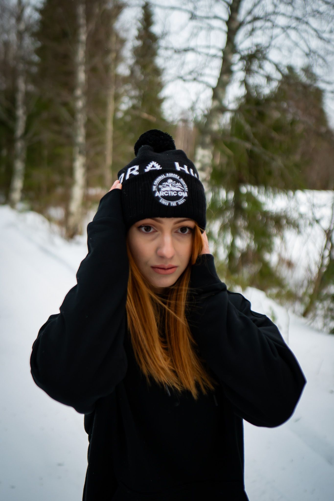 Close-up of woman adjusting black Arctic GM beanie with embroidered logo