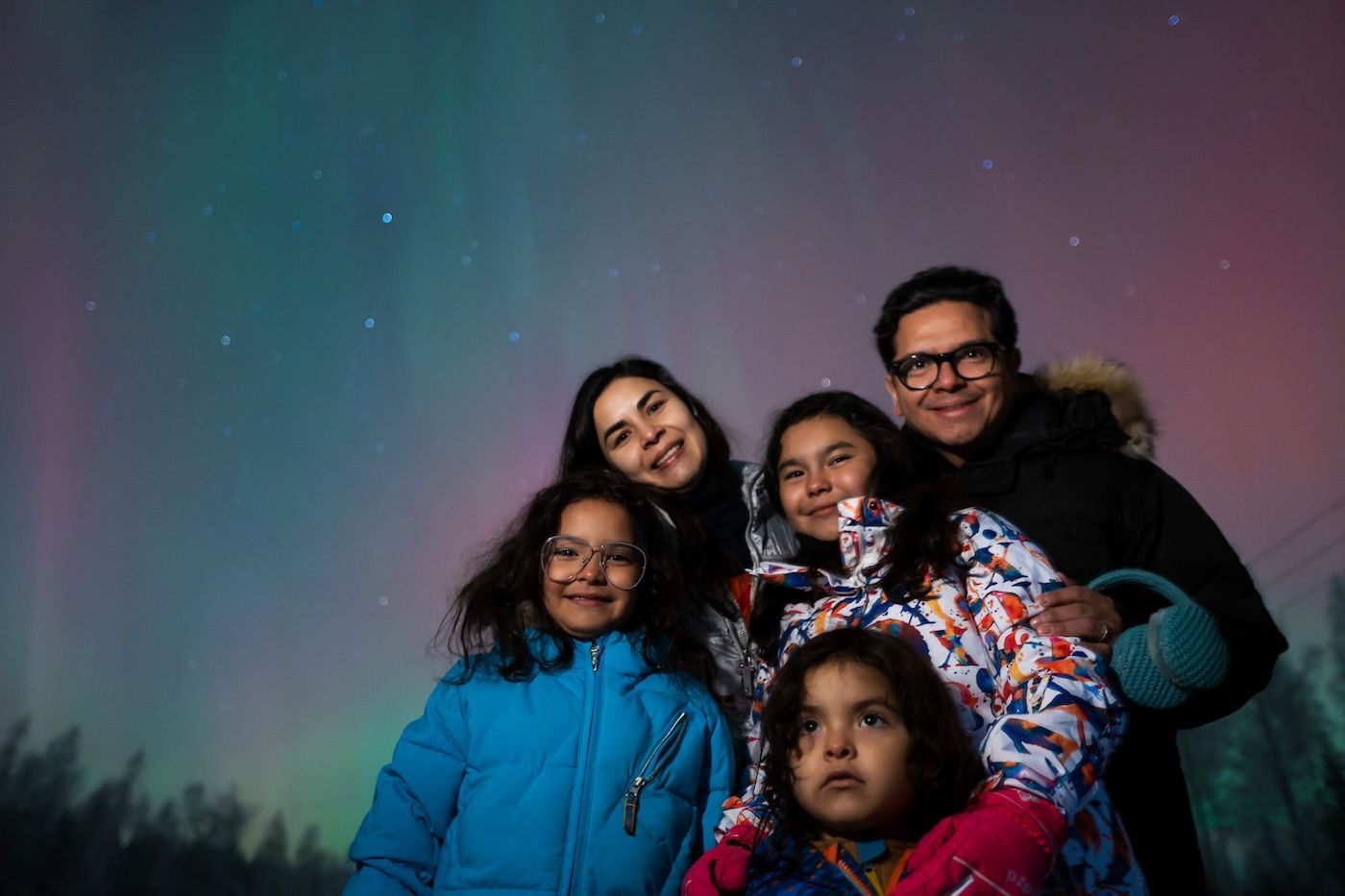 Family smiling under green skies on a Northern Lights experience with Arctic GM in Lapland