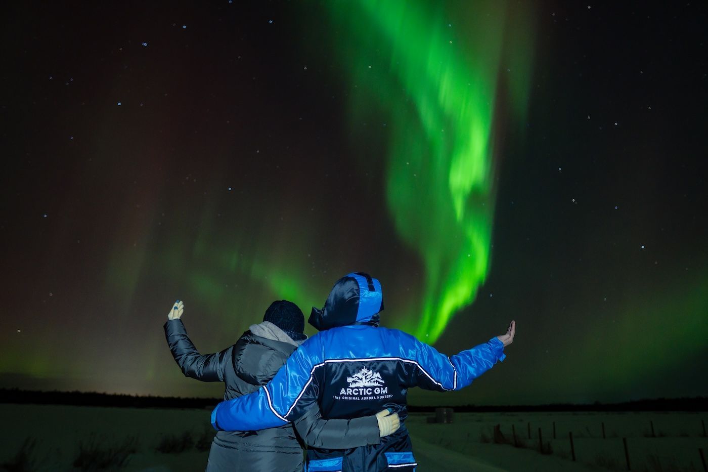 Couple embracing under vivid Aurora sky on an Arctic GM night tour in Lapland