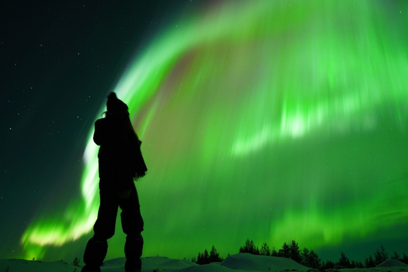 Silhouette of guest photographing vibrant Aurora on Arctic GM night tour in Levi