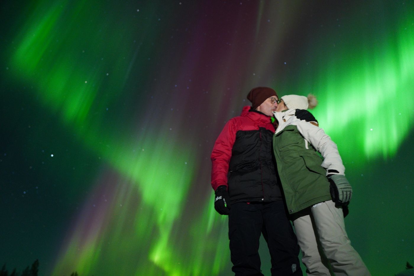 Guests hugging beneath the green Northern Lights on a winter tour in Finnish Lapland