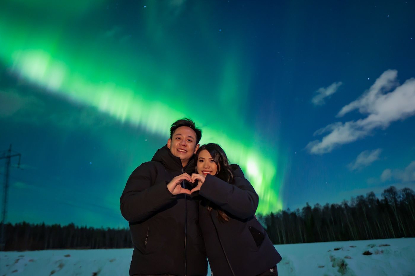 Guest forming heart with hands under the Northern Lights on Arctic GM adventure