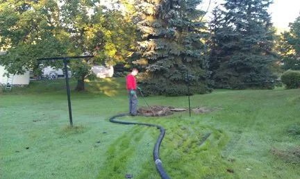 A man is standing in a yard with a hose.