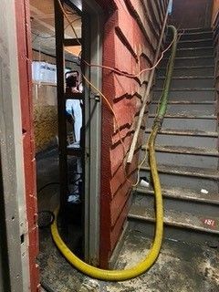 A yellow hose is hanging from the side of a building next to stairs.