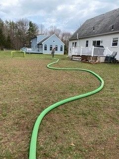 A green hose is laying in the grass in front of a house.
