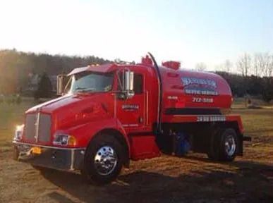 A red septic tank truck is parked in a field.
