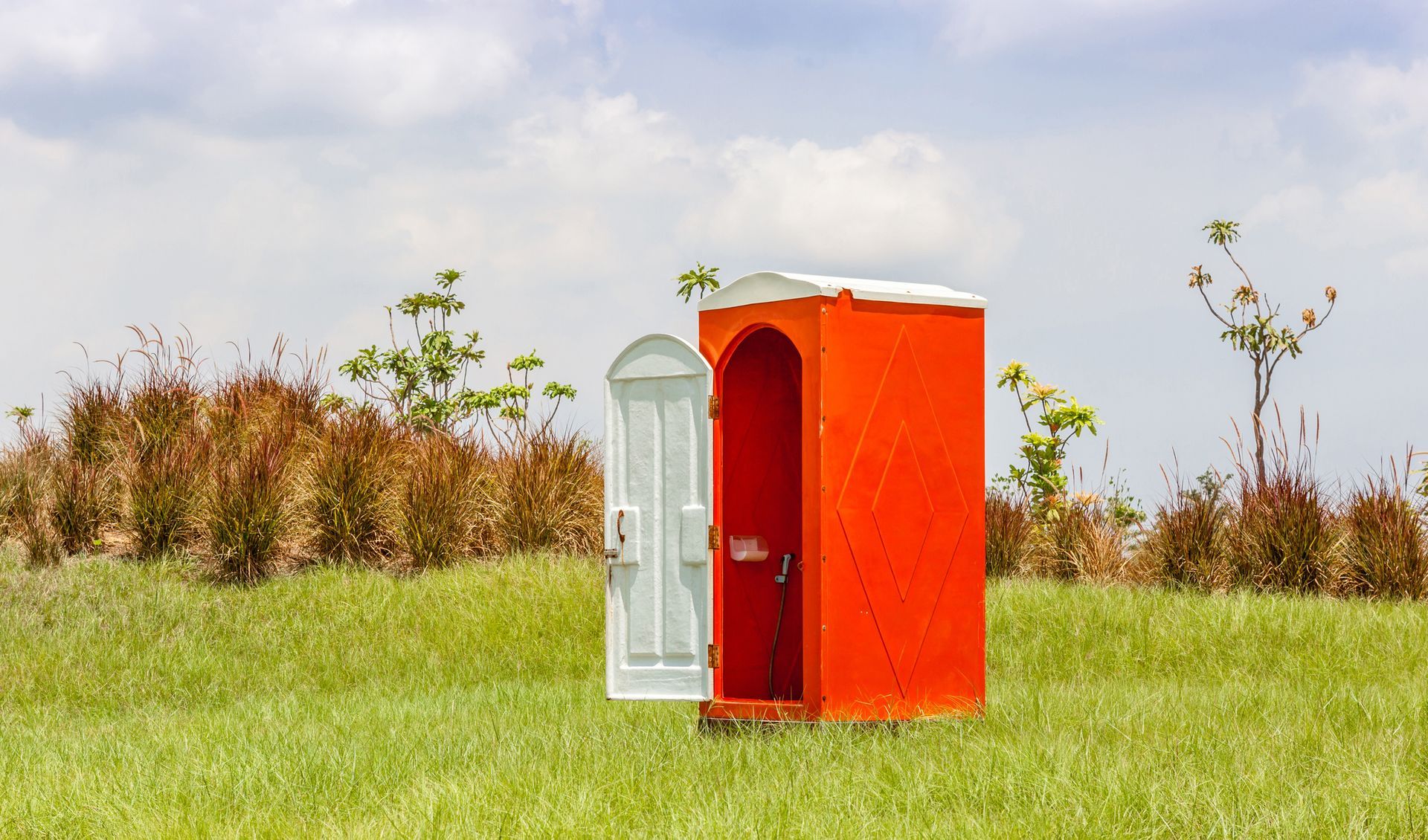 a red porta potty stands with door open in a backyard