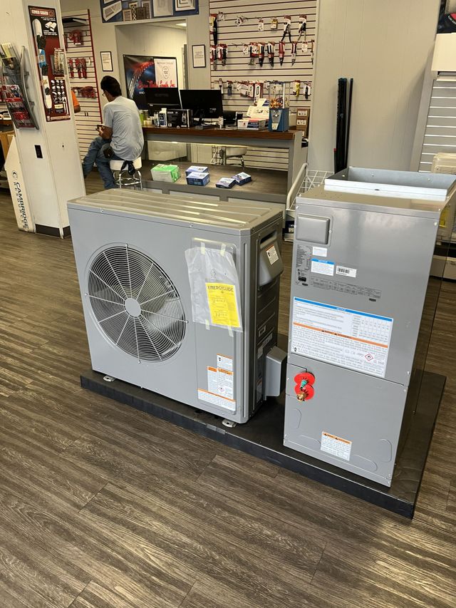 Office with HVAC units, desk, and wall posters; a person works behind the counter.
