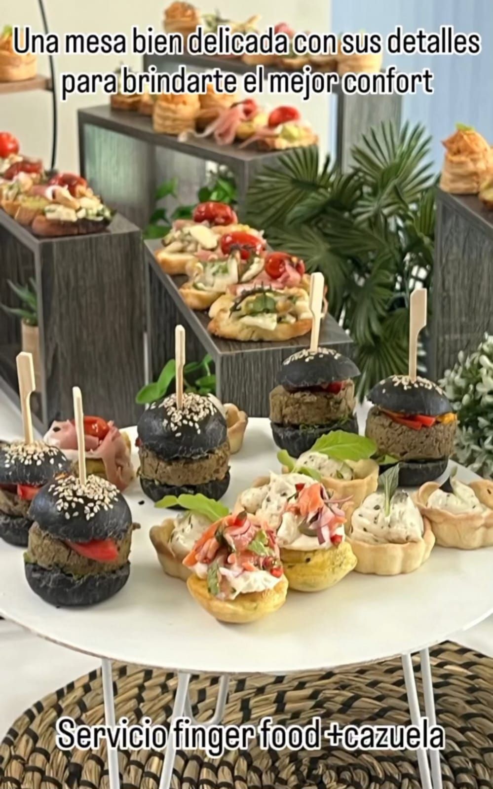 Una mesa con diversos aperitivos, incluyendo minihamburguesas, en bandejas escalonadas. El texto dice "Servicio de aperitivos".