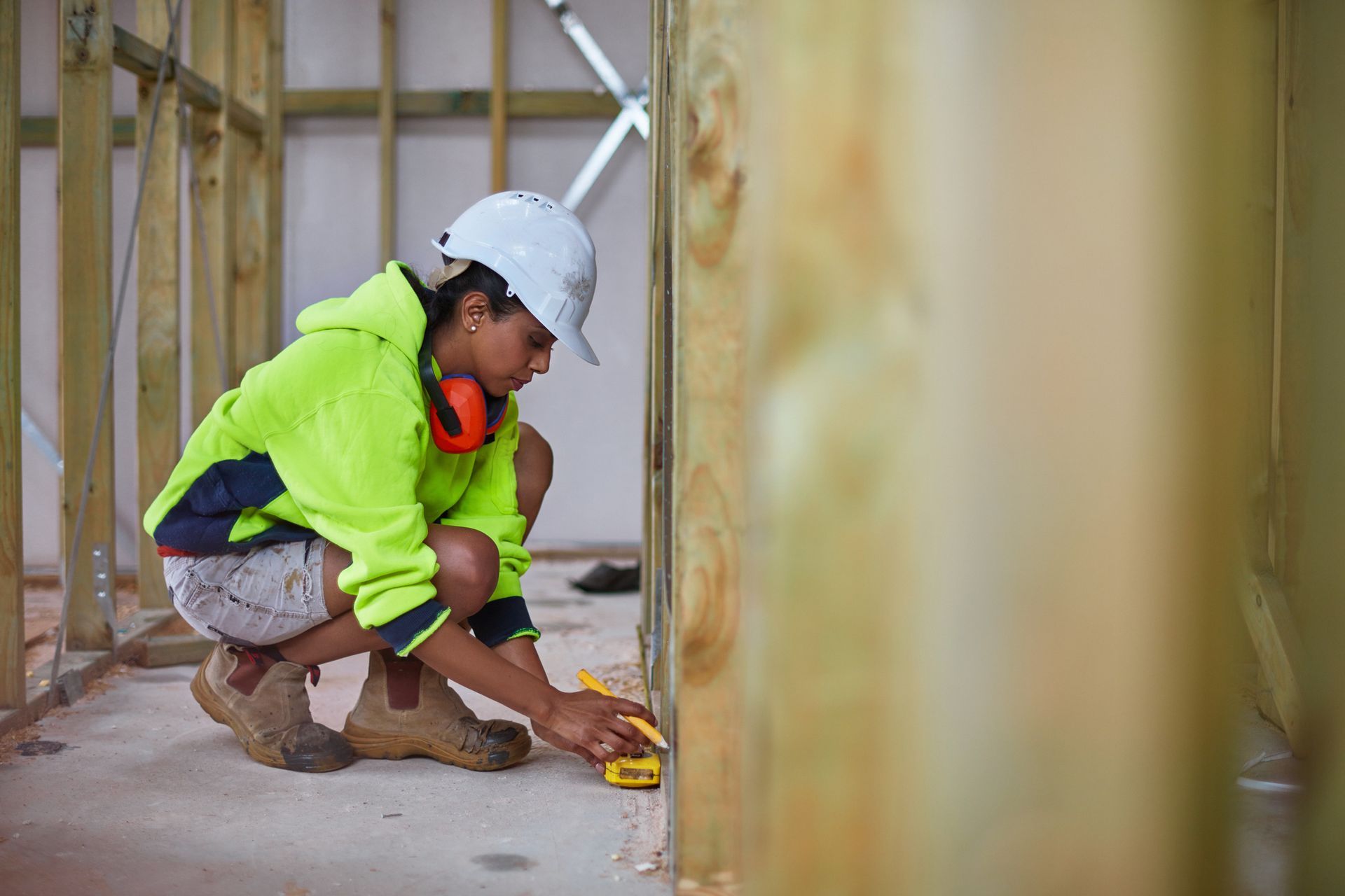 A construction worker is measuring a wall with a tape measure.