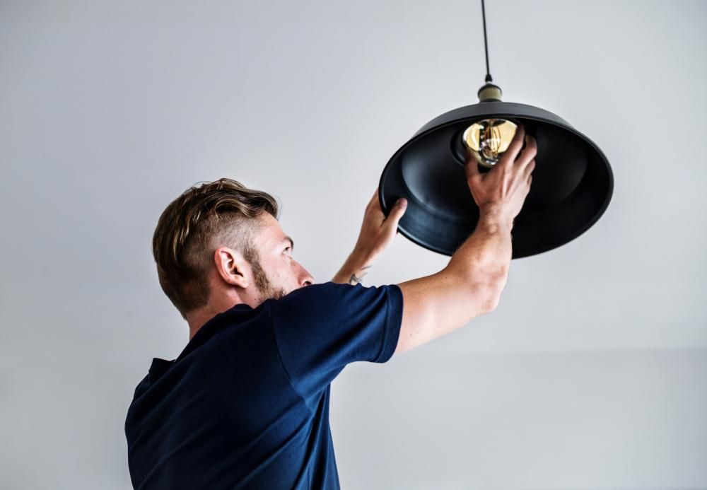 A Man Is Installing A Light Fixture On A Ceiling — Canberra Handyman Solutions In Wanniassa, ACT
