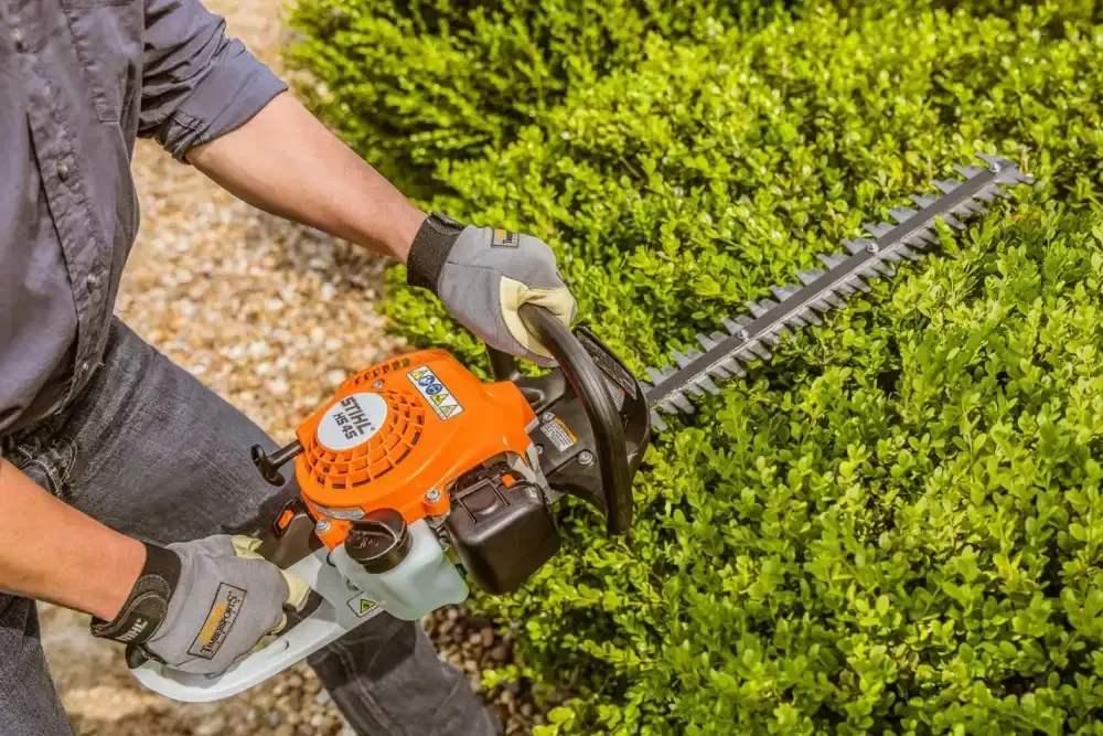 A Man Is Cutting a Bush with A Hedge Trimmer — Stihl Shop Grafton in Grafton, NSW