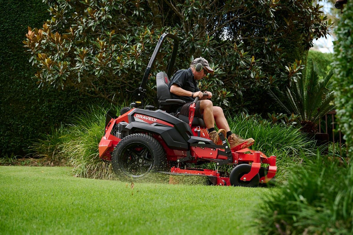 A Man Is Riding a Red Lawn Mower on A Lush Green Lawn — Stihl Shop Grafton in Woolgoolga, NSW