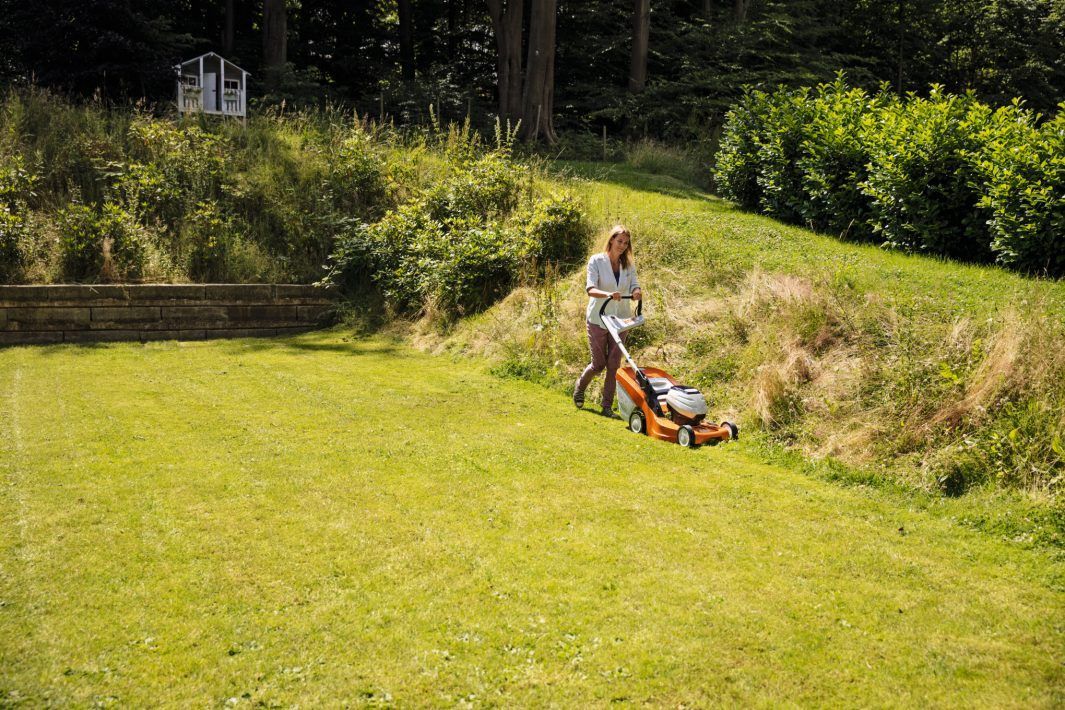 A Man Is Mowing a Lush Green Lawn with A Lawn Mower — Stihl Shop Grafton in Grafton, NSW