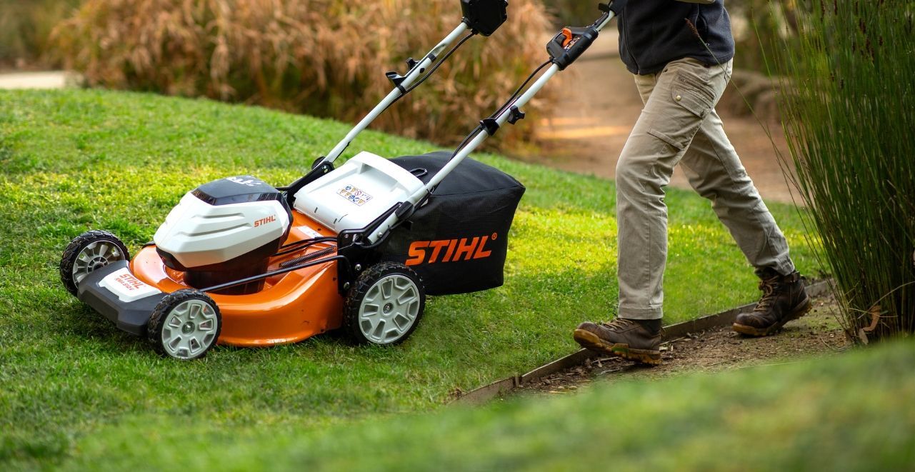 A Man Is Pushing a Lawn Mower on A Lush Green Lawn — Stihl Shop Grafton in Grafton, NSW