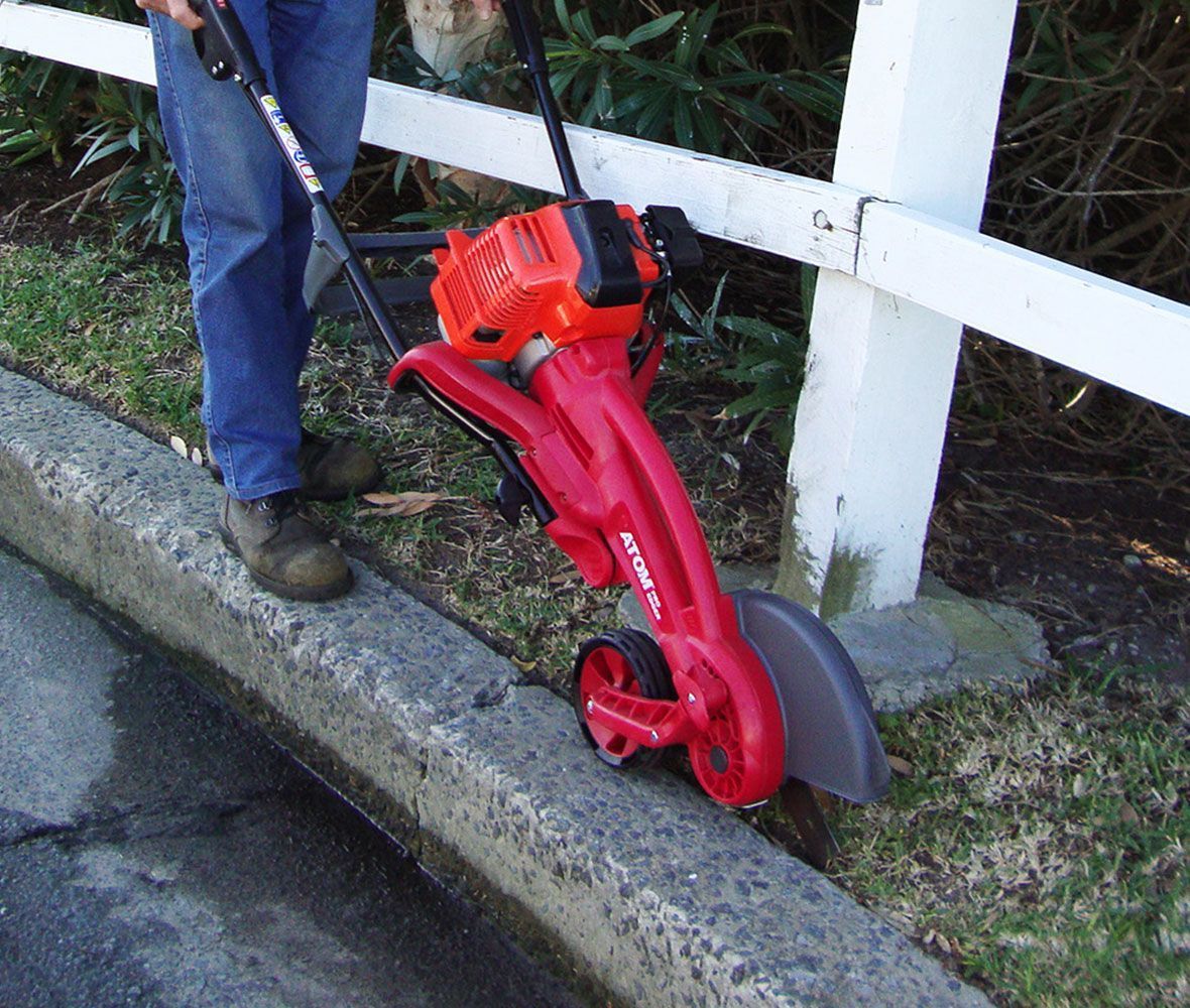 A Person Is Using a Red Lawn Mower on A Curb — Stihl Shop Grafton in Grafton, NSW