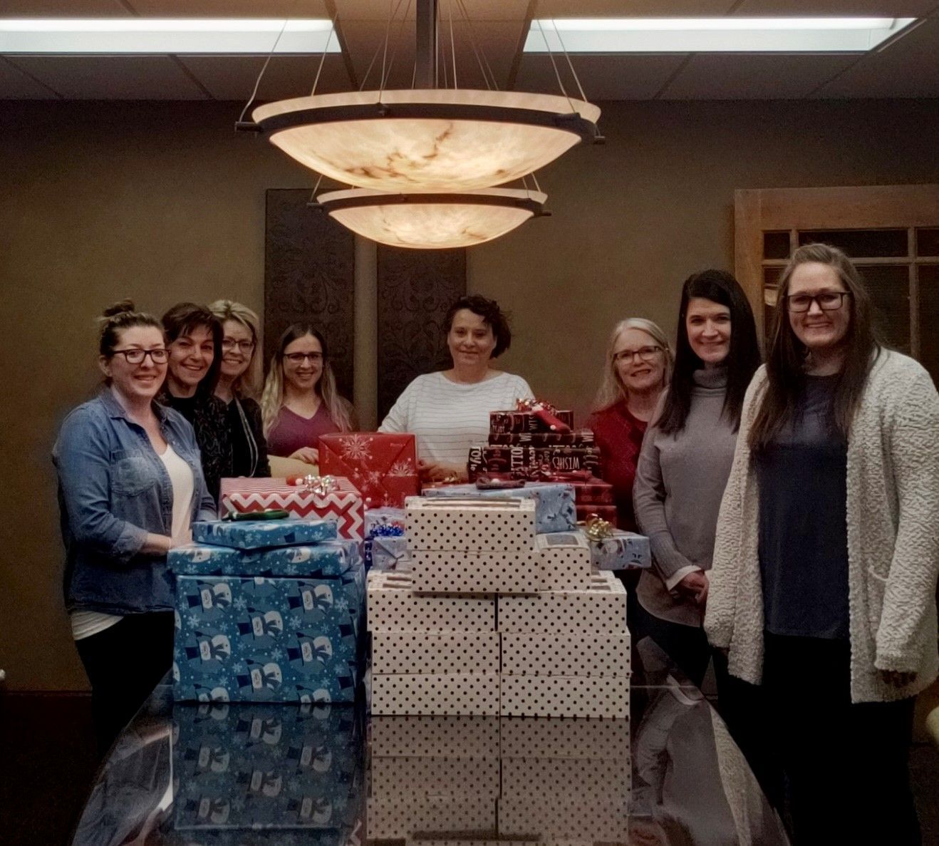 Group of women smiling with a table full of wrapped gifts indoors.