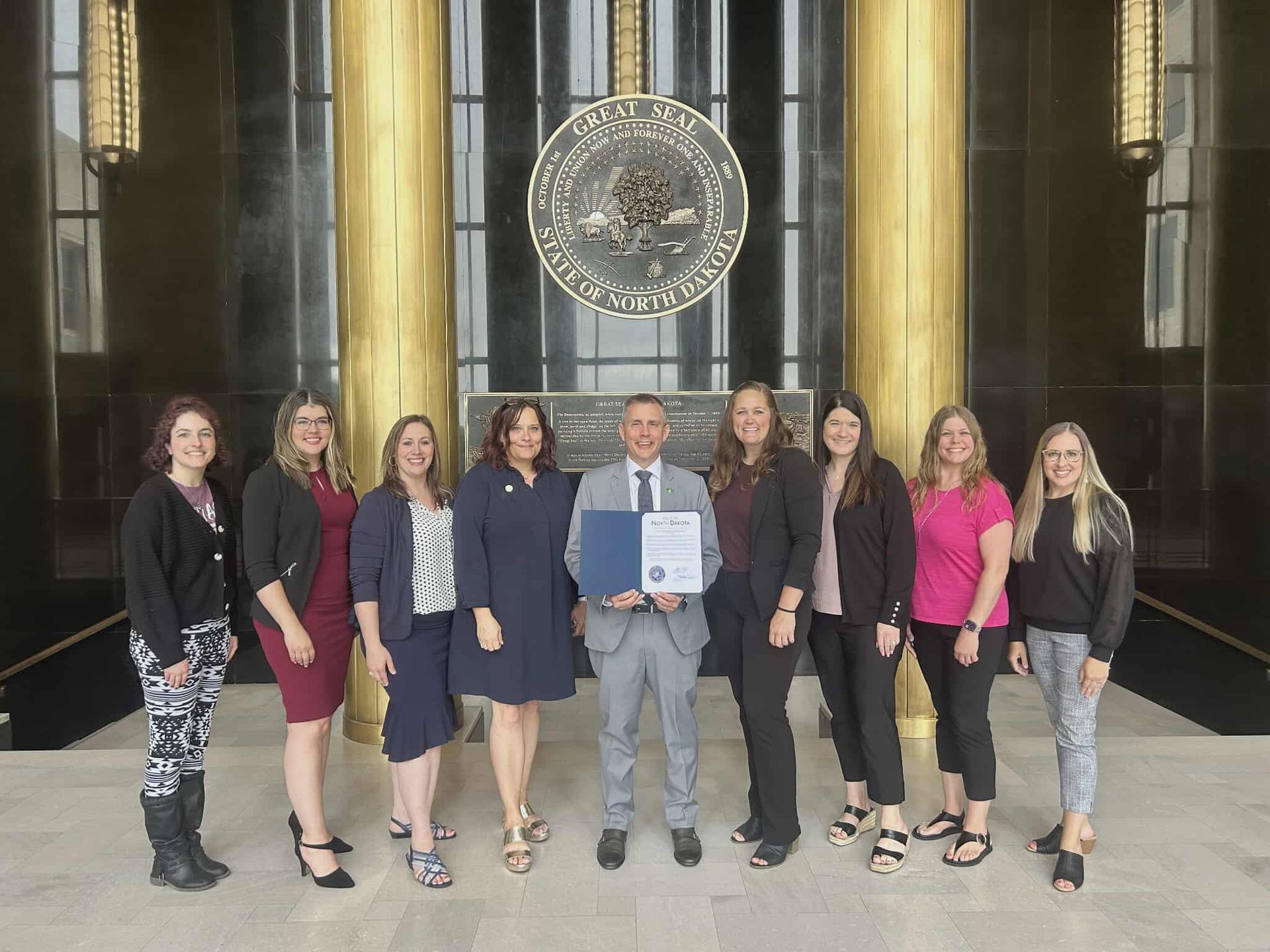 Group of people standing in a building, holding a document in front of a seal.