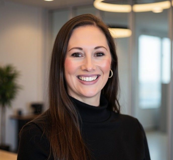 Woman in navy blazer and patterned blouse smiles in front of bookshelves.