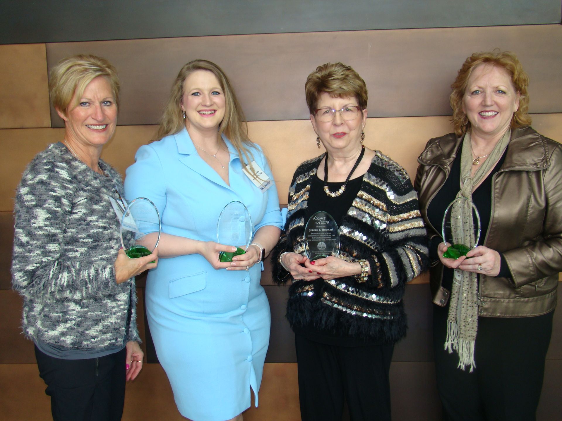 Four women smiling, holding green awards, posing in front of a brown patterned wall.