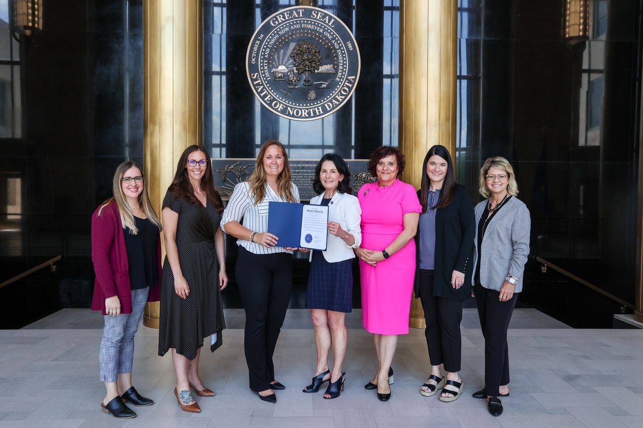 Group of seven women pose holding documents, in front of government building.