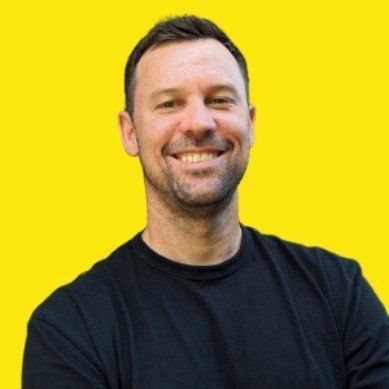 A man in a black shirt is smiling with his arms crossed.