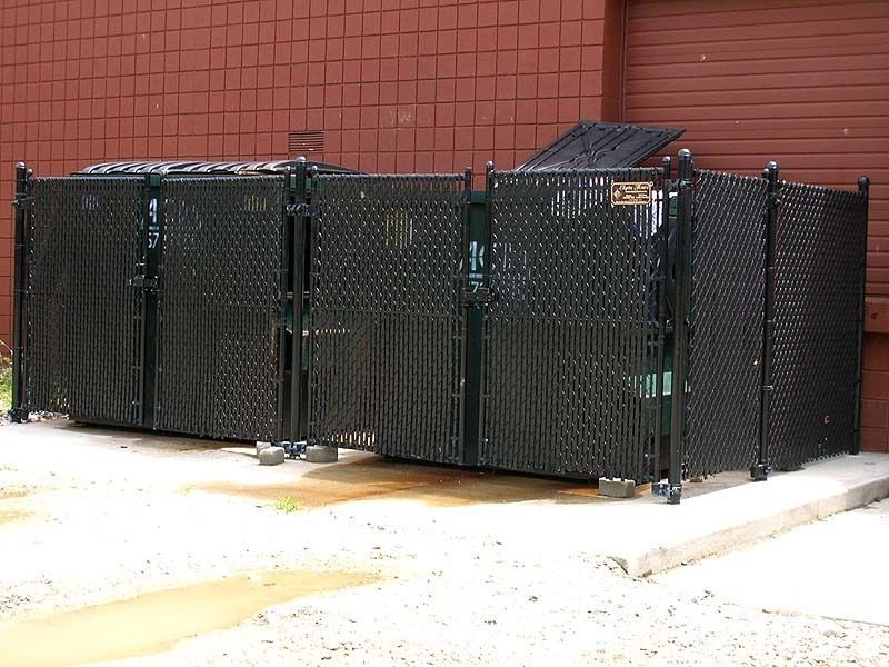 Black metal dumpster enclosure with two swinging gates, against a brick building.