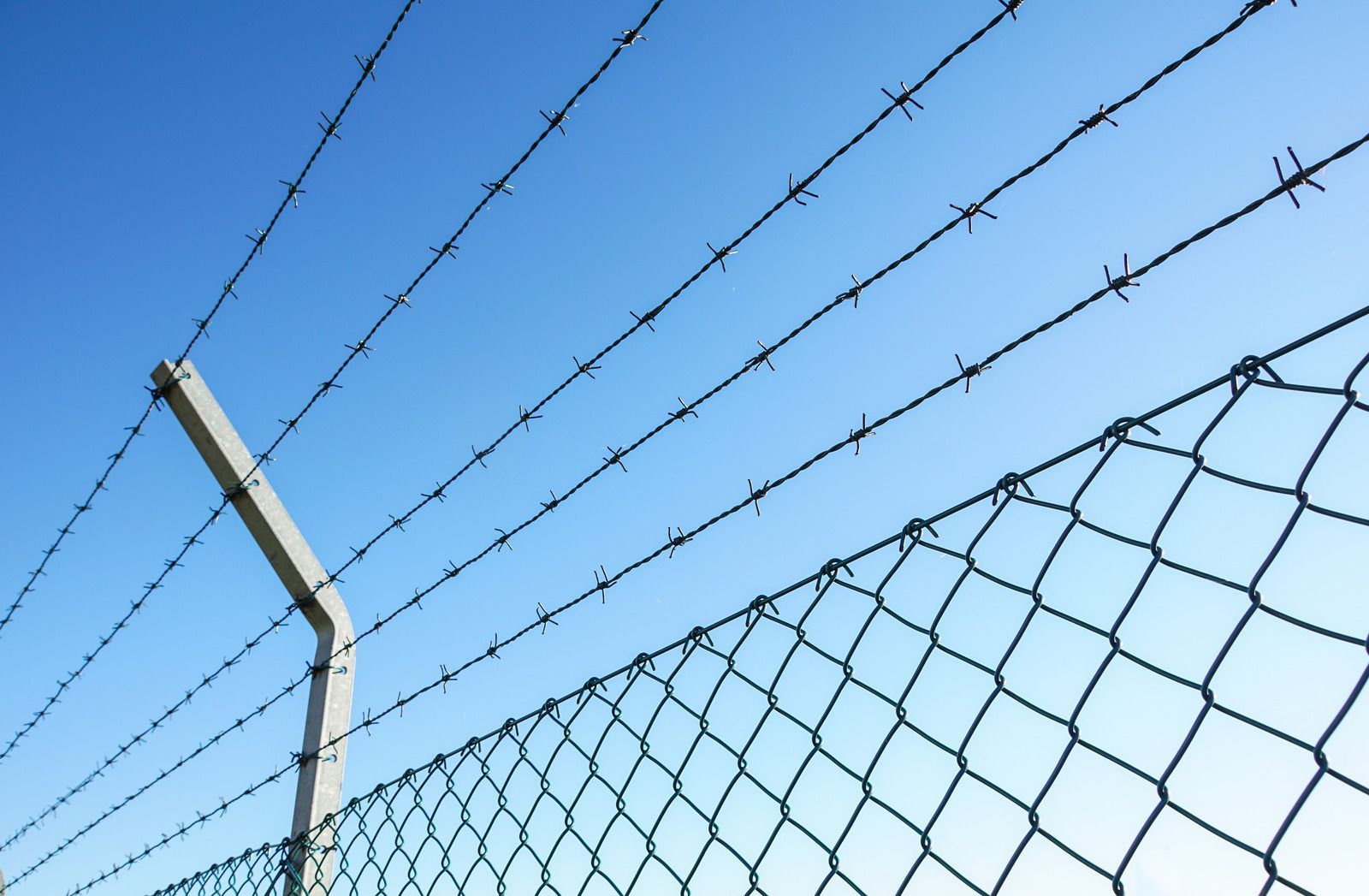 Barbed wire and chain-link fence against a clear, blue sky.