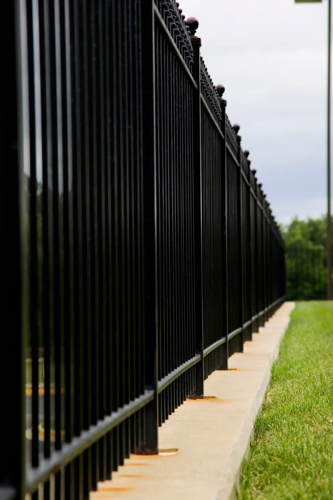 Black metal fence bordering a strip of green grass and concrete.