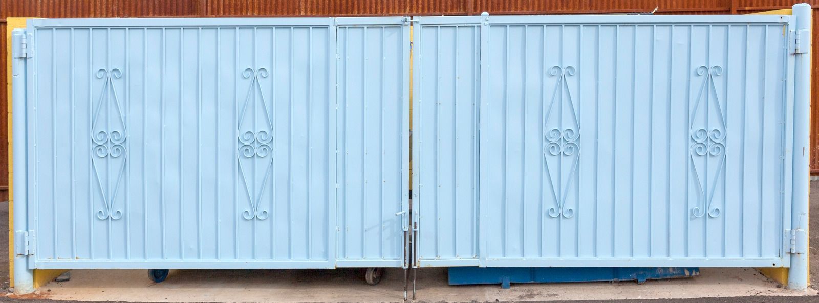 Light blue metal gate with decorative diamond shapes, standing outdoors.