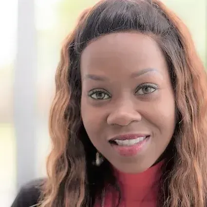 A woman with long hair and a red turtleneck is smiling for the camera.