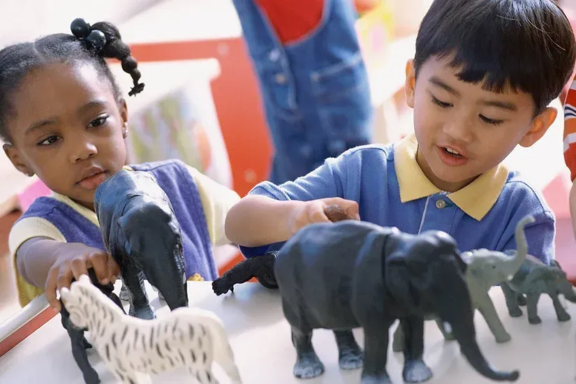 A boy and a girl are playing with plastic animals on a table