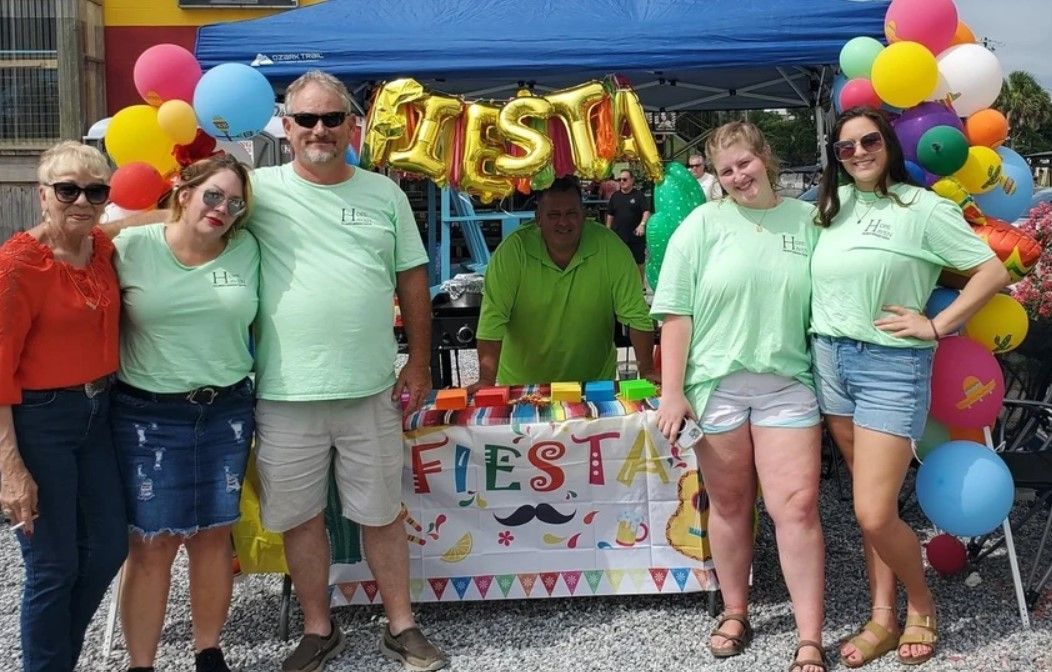A group of people standing around a table with balloons and a sign that says fiesta.