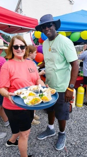A man and a woman are standing next to each other holding a tray of food.