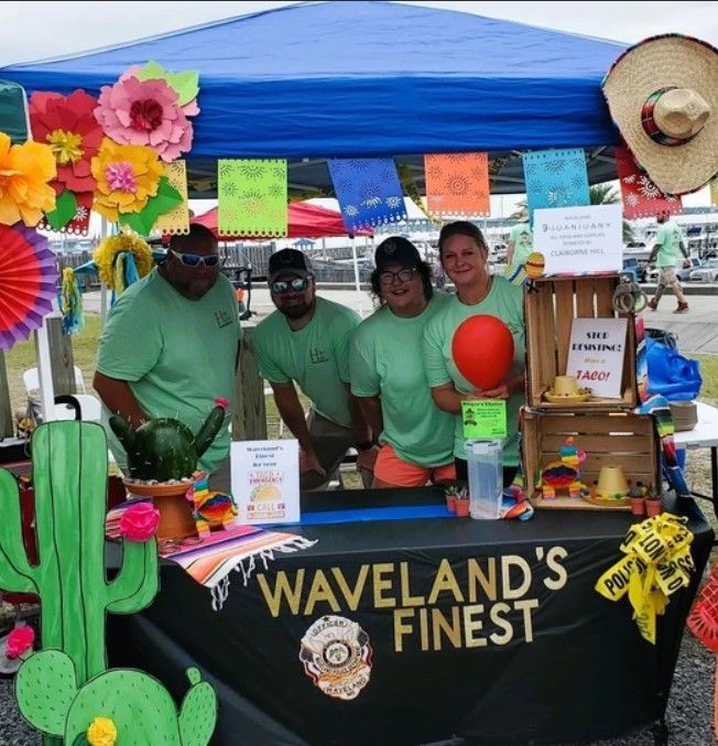 A group of people standing around a table that says waveland 's finest