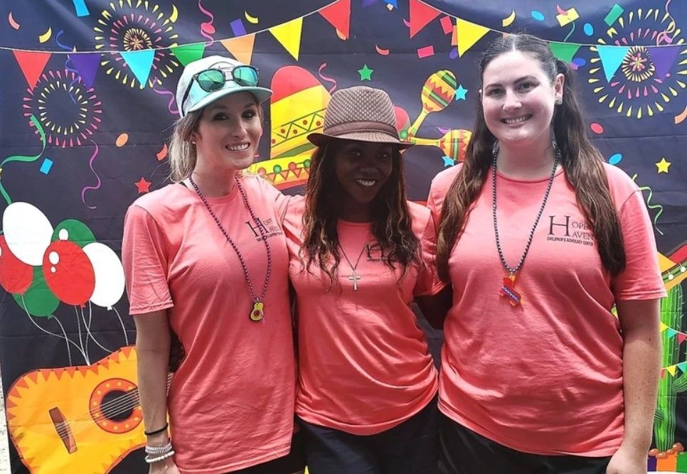 Three women wearing pink shirts are posing for a picture