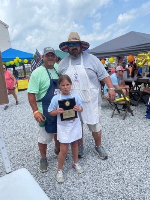 A little girl is holding a plaque with two men standing behind her