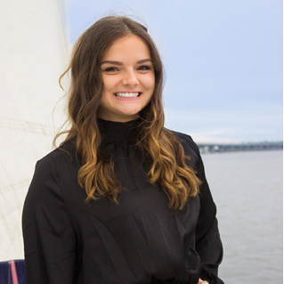 A woman in a black shirt is smiling in front of a body of water.