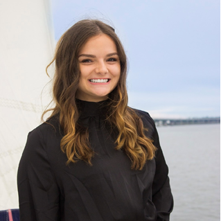 A woman in a black shirt is smiling in front of a body of water.