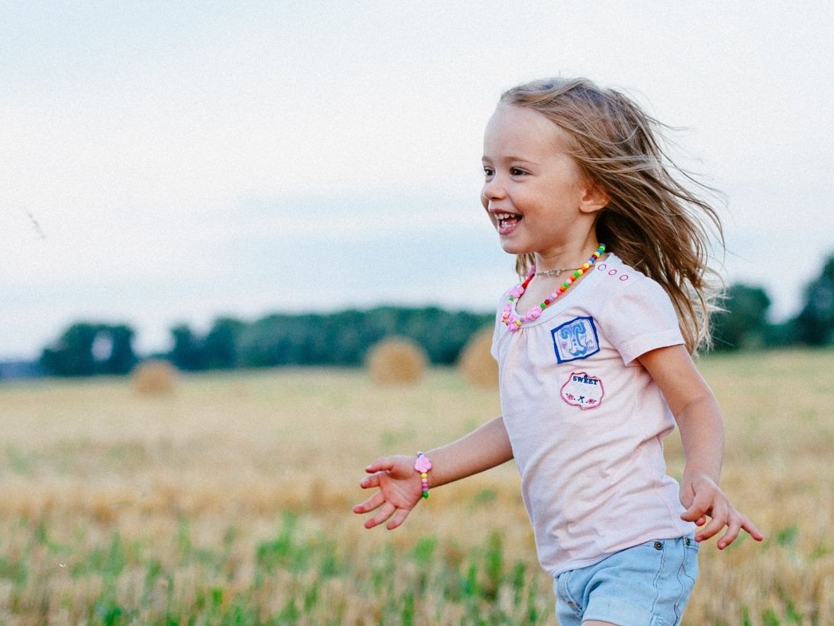 A little girl is running in a field of hay.