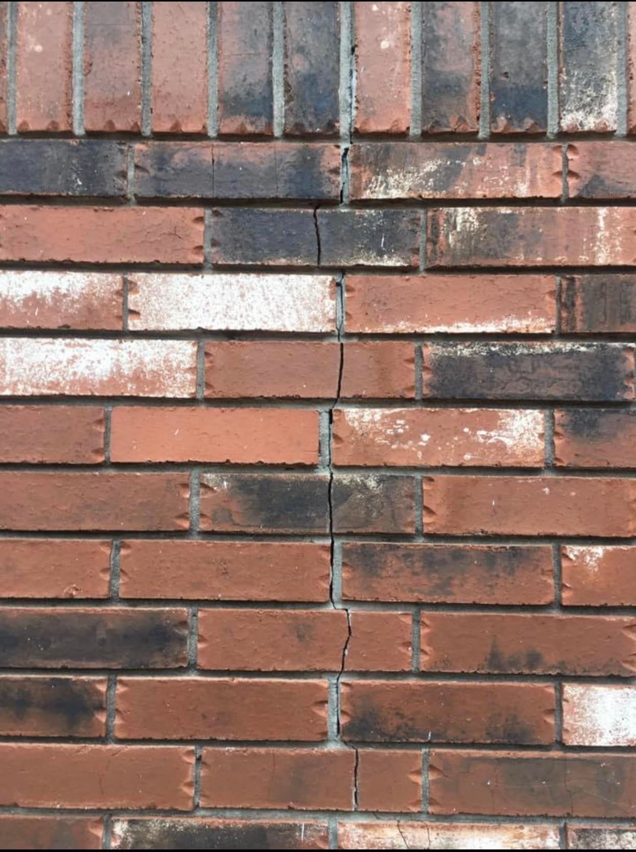 Brick wall with vertical cracks, alternating red and black bricks.