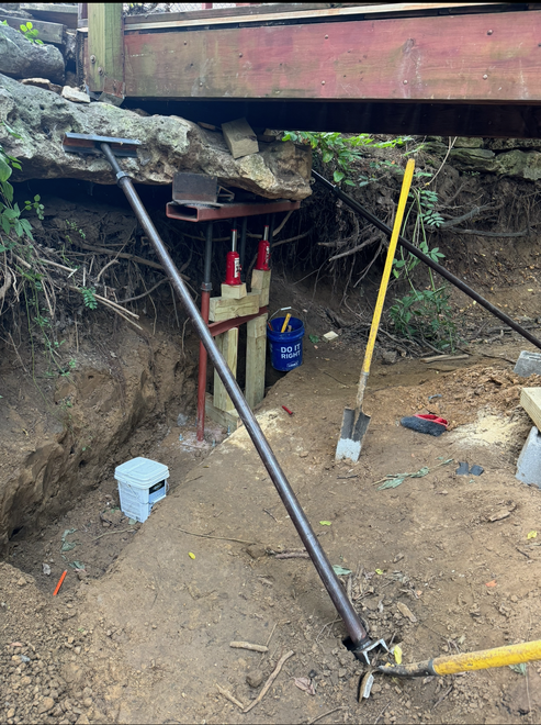Construction site with a bridge being supported by jacks and beams, a trench, and tools.