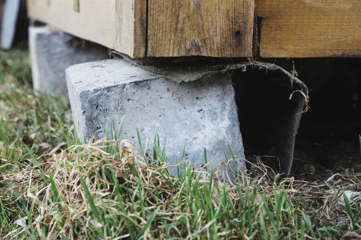 Wooden structure supported by uneven concrete blocks on grassy ground.