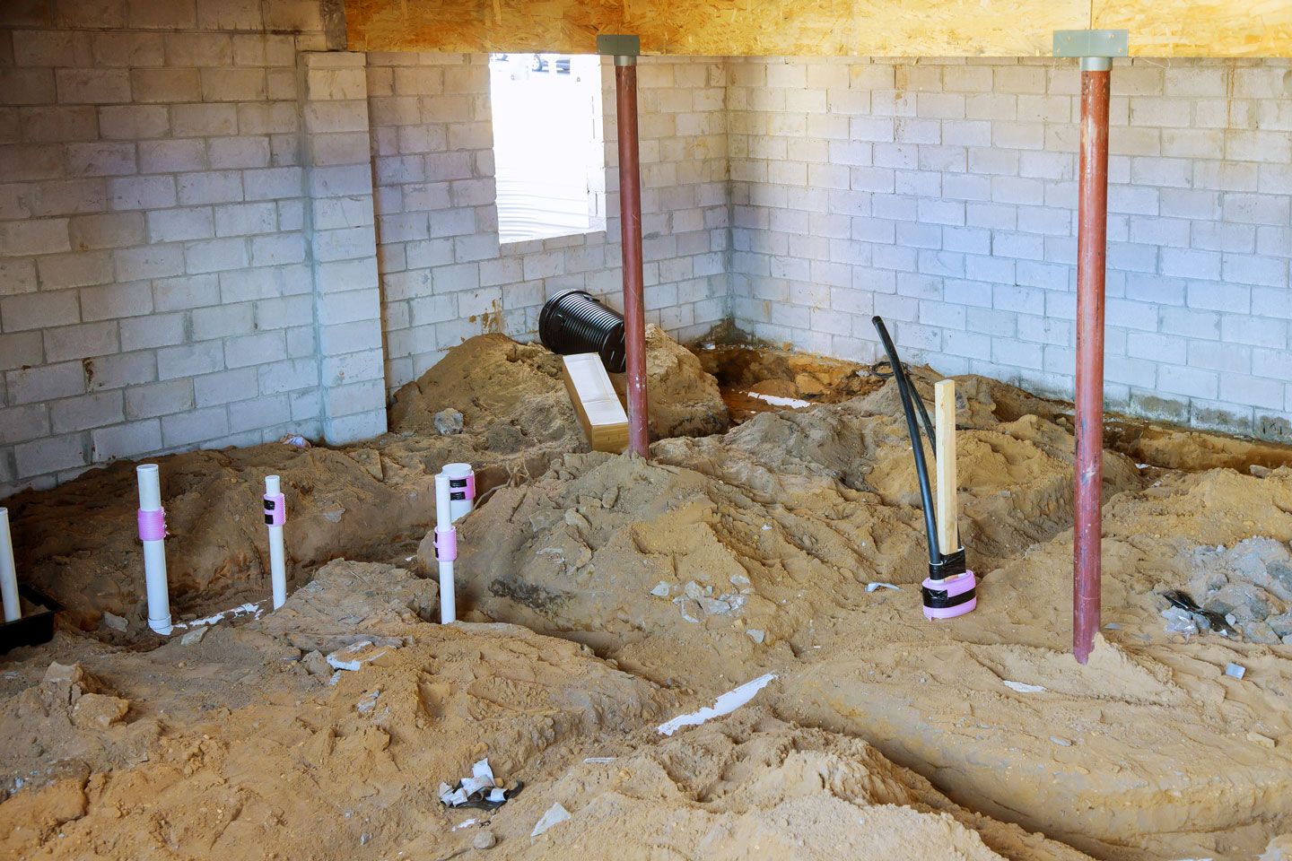 Underground plumbing and copper pipes in unfinished basement with sand and cinder block walls.