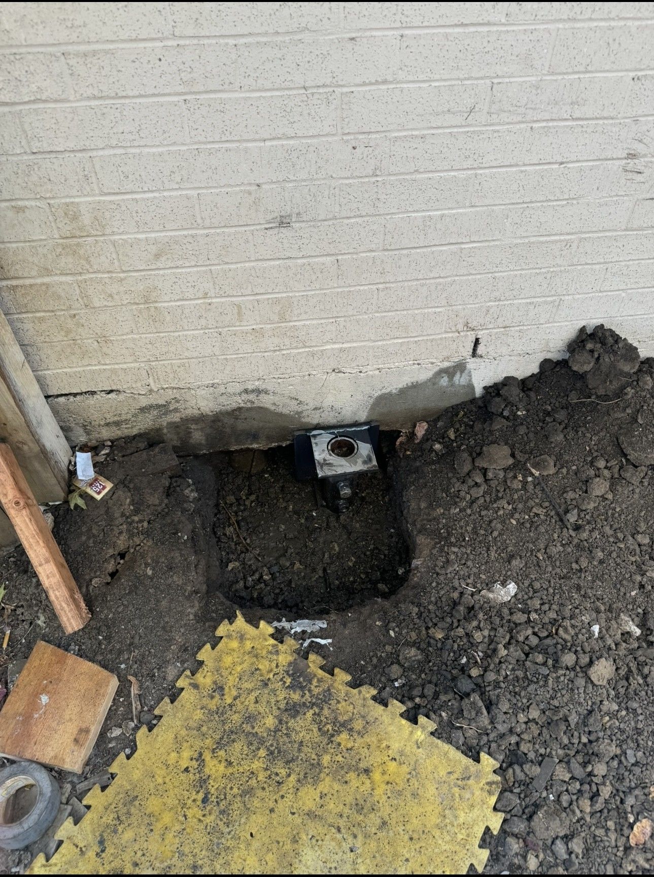 Hole dug in dirt near concrete wall, revealing a pipe fitting.